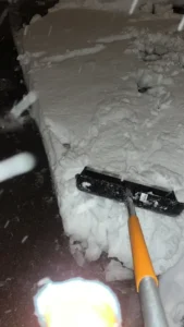 Schneeschaufel im Einsatz auf einem verschneiten Gehweg bei Nacht.